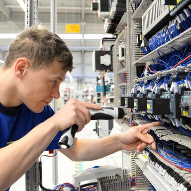 Ein junger Mann arbeitet an einem Stromkasten an Kabeln.